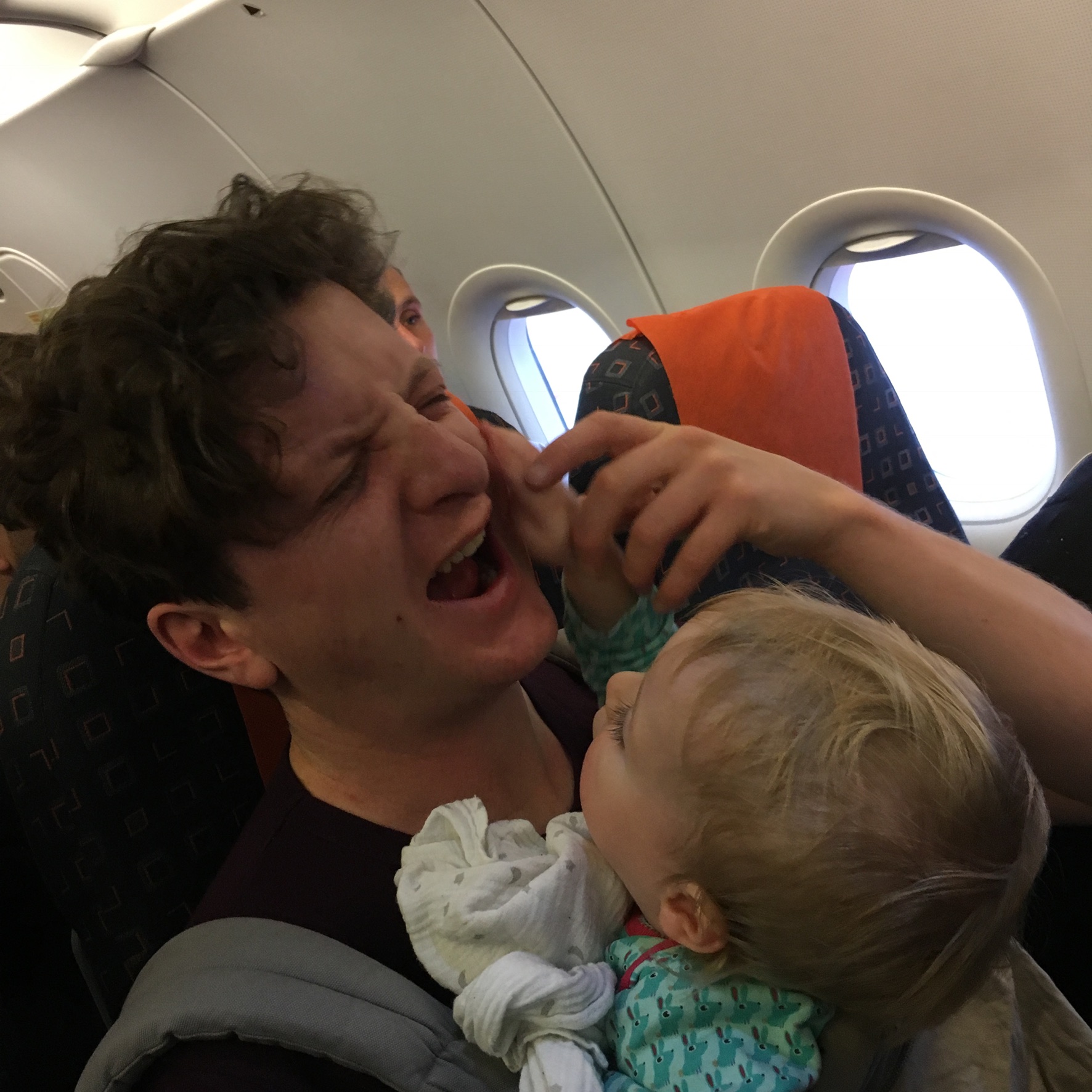 A baby grabs her father's face on a plane