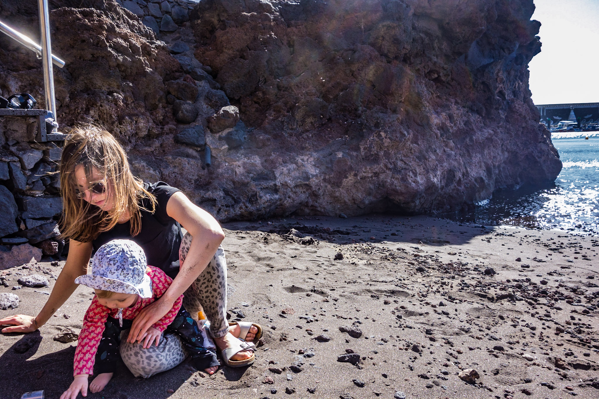 A woman and a baby play on a black sand beach