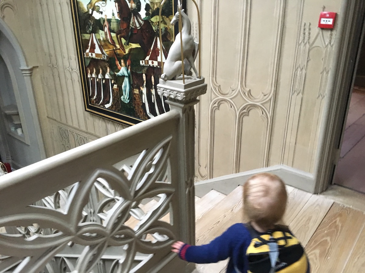 A toddler wearing a bag that looks like a bee at the top of the stairs at the Gothic masterpiece Strawberry Hill House