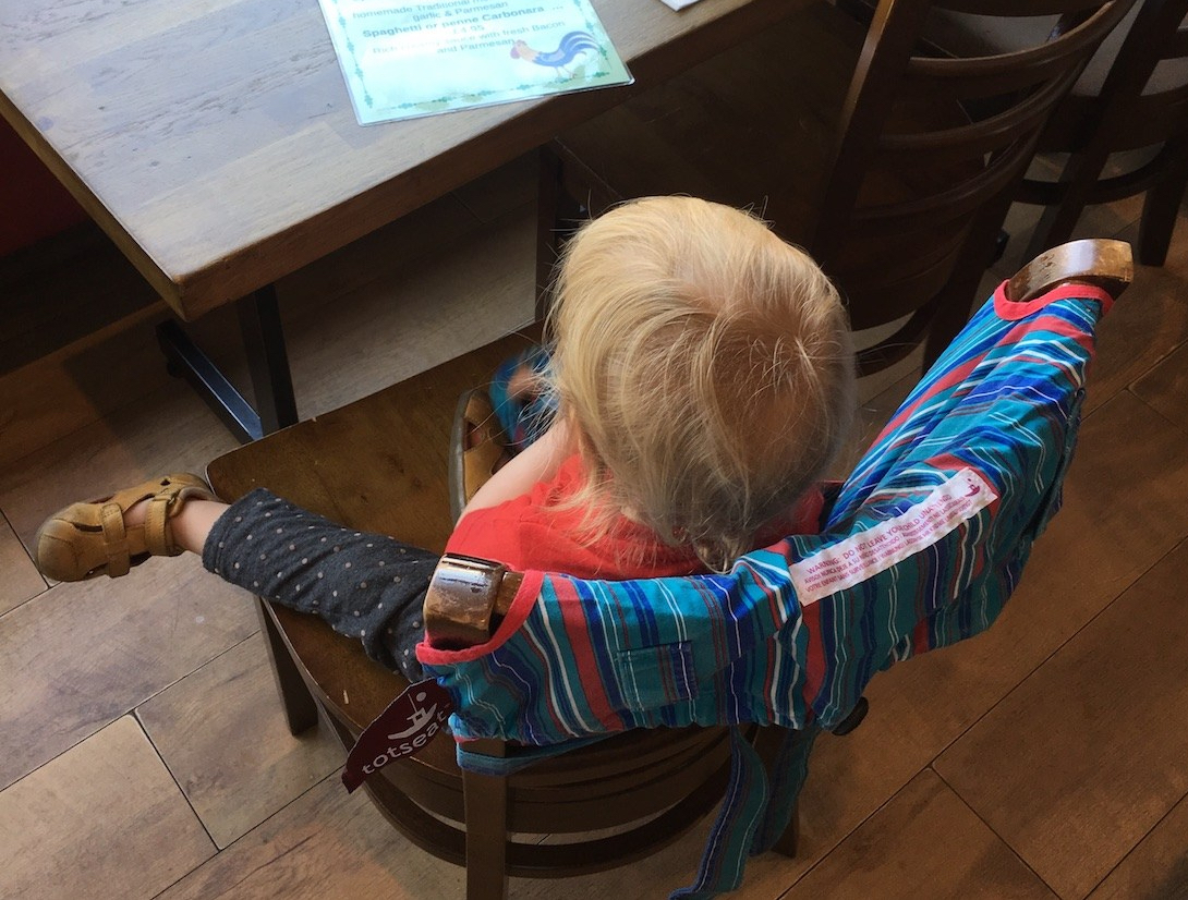 Toddler in a portable high chair at a table in a restaurant