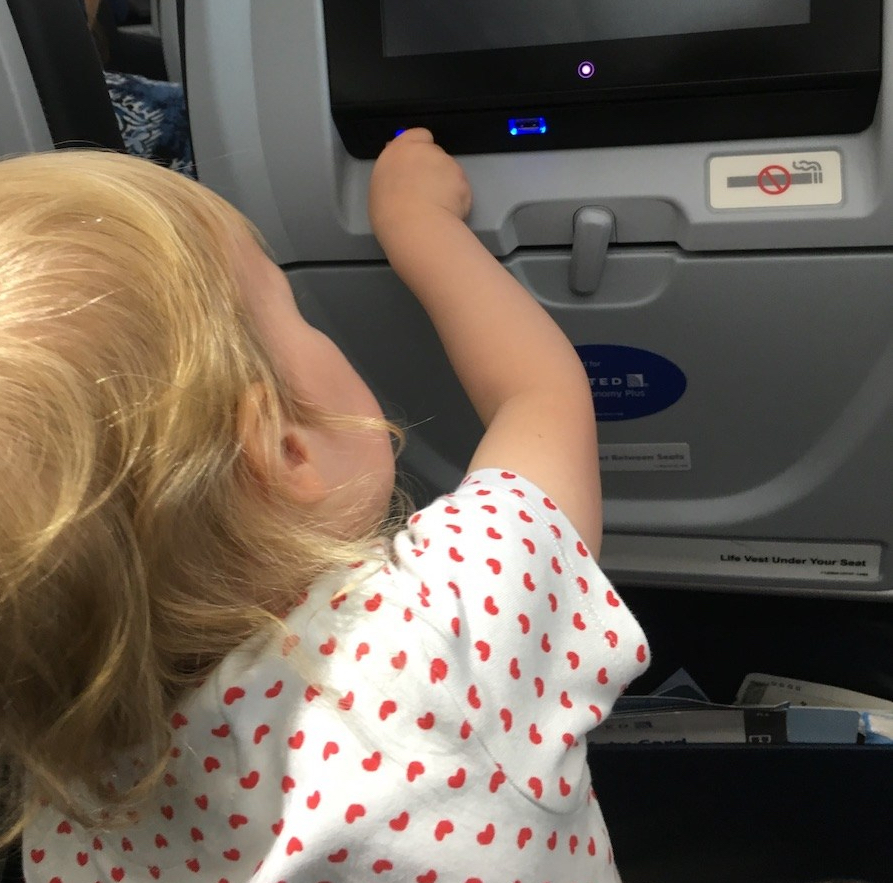 A toddler plugs in a phone charge on a plane
