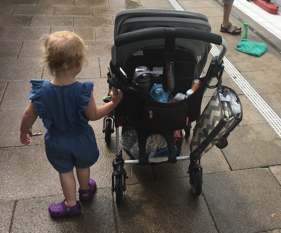The toddlers walks beside a laden pushchair