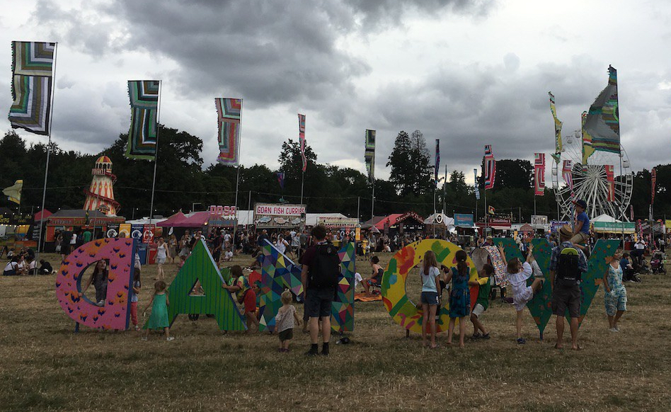 Adults and children play on the WOMAD sign at the music festival